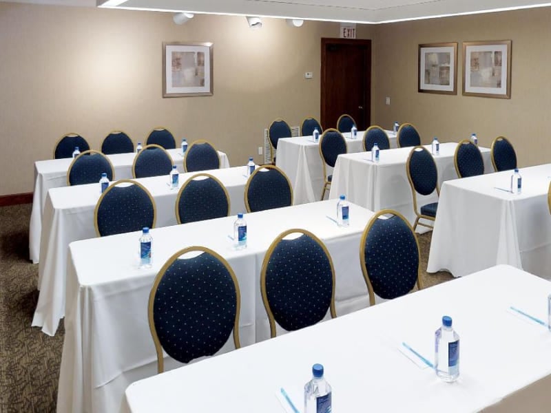 A meeting room with white tables, blue chairs, and framed pictures on the walls.